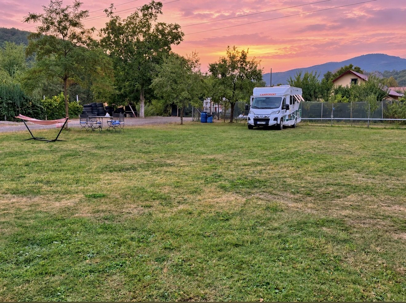Ein Wohnmobil auf der Wiese unter rosa Abendhimmel, mit einer Hängematte im Vordergrund